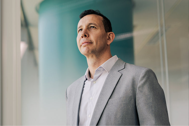 Man in gray suit looking thoughtfully out a window in an office setting.